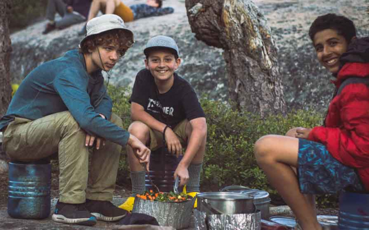 three young people use camping stoves to prepare food on an outward bound expedition 